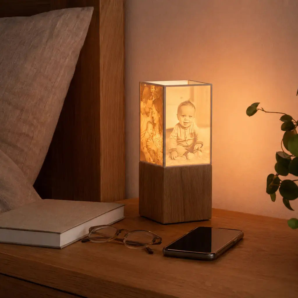 Warm leuchtende ArtLight Fotolampe auf einem Nachtkästchen neben Buch, Brille und Smartphone